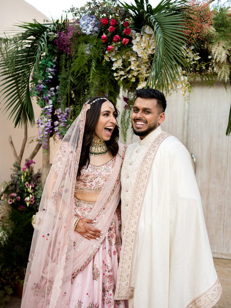 Bride laughing beside groom in ivory sherwani and pink lehenga at Athens Riviera wedding venue.