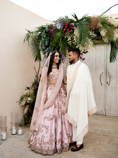 Bride and groom posing under tropical floral installation at Private House Island Resort Indian wedding.