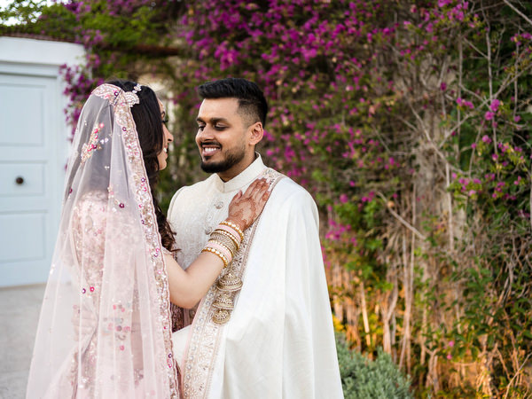 Bride adjusting veil while groom smiles during Indian wedding portraits in Athens Riviera.