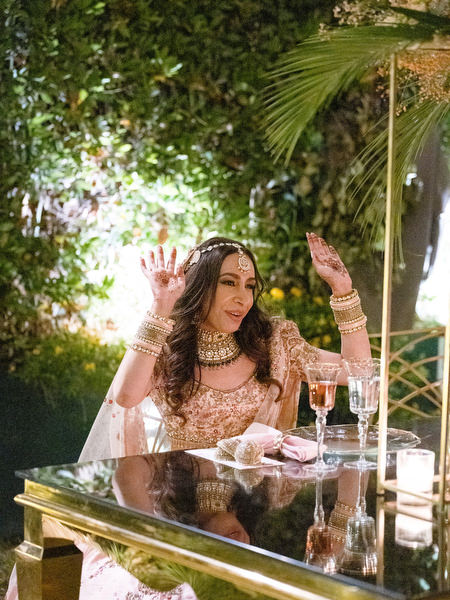 Bride in pink lehenga seated at reception table during sunset at Athens Riviera Indian wedding.