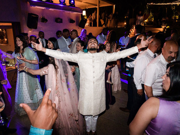 Groom dancing with arms raised at luxury Indian wedding party in Athens Riviera.