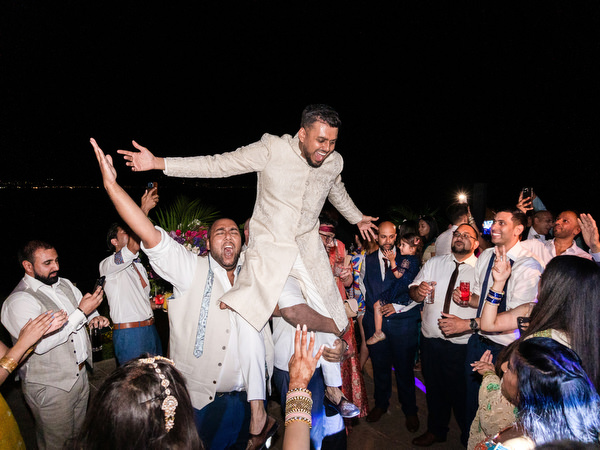 Guests lifting groom onto shoulders during Indian wedding party in Athens Riviera.