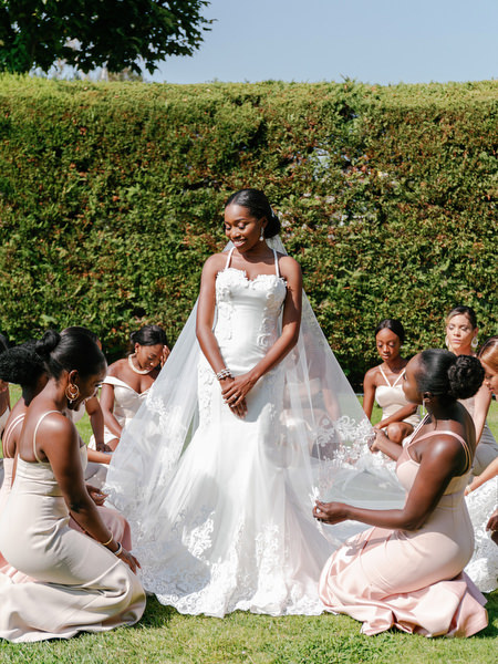 Bride surrounded by bridesmaids in blush dresses during luxury Nigerian wedding ceremony preparations in Athens.