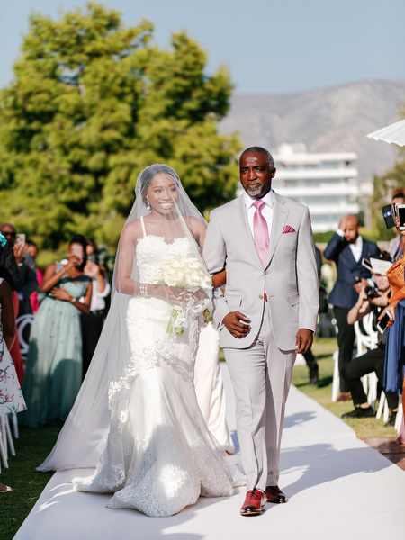 Bride walking down white aisle with her father during luxury Nigerian wedding ceremony at Ble Azure on the Athens Riviera.