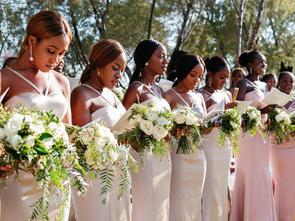 Bridesmaids in coordinated blush gowns holding white bouquets at Ble Azure luxury Nigerian wedding ceremony in Athens.
