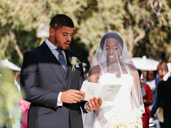 Bride and groom reading vows under white floral arch at Ble Azure Nigerian destination wedding in Greece.