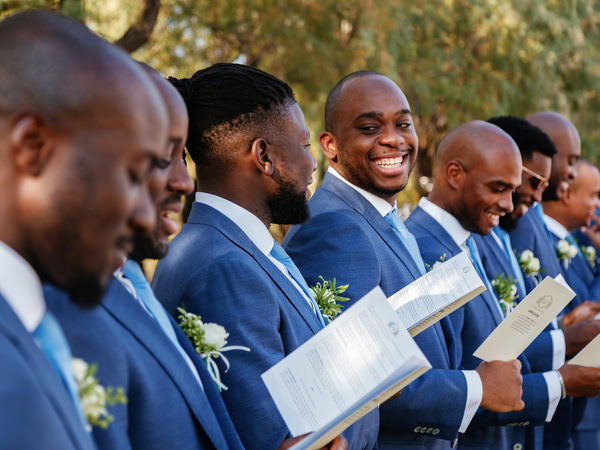 Groomsmen in blue suits holding ceremony programs during luxury Nigerian wedding at Ble Azure Athens Riviera.