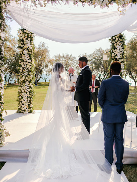 Bride and groom standing beneath white draped floral altar at Ble Azure ceremony on the Athens Riviera.