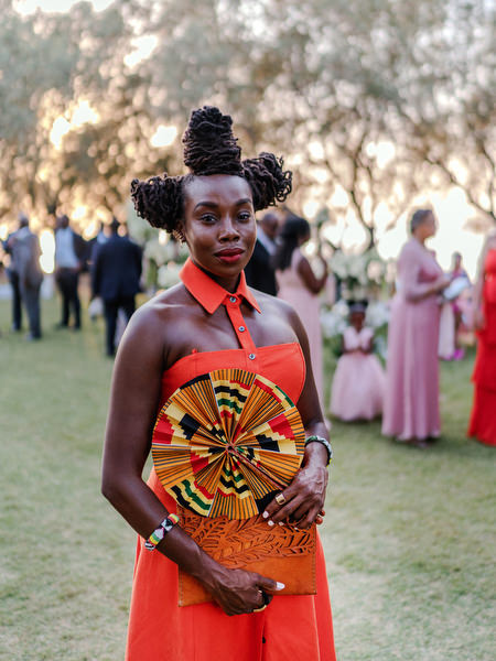 Female guest in bold orange dress at luxury Nigerian wedding ceremony at Ble Azure in Athens Greece.