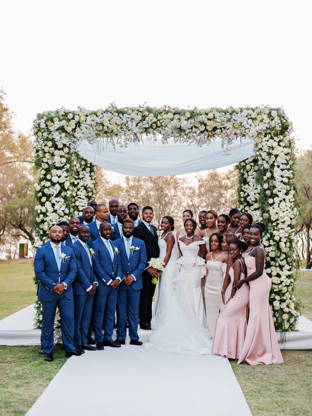Large bridal party portrait under floral arch at Ble Azure during 400-guest Nigerian wedding in Athens Greece.