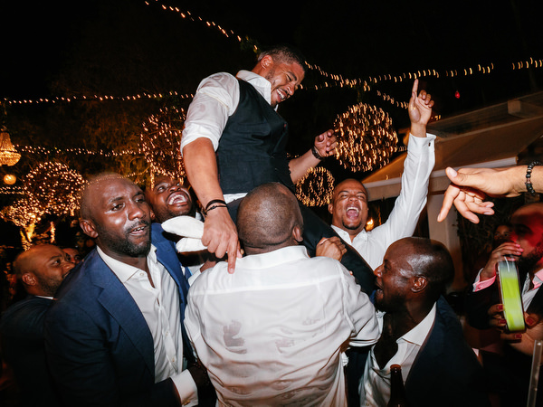 Groom lifted by friends on dance floor at Island Resort The Residence Nigerian wedding reception in Athens Riviera.