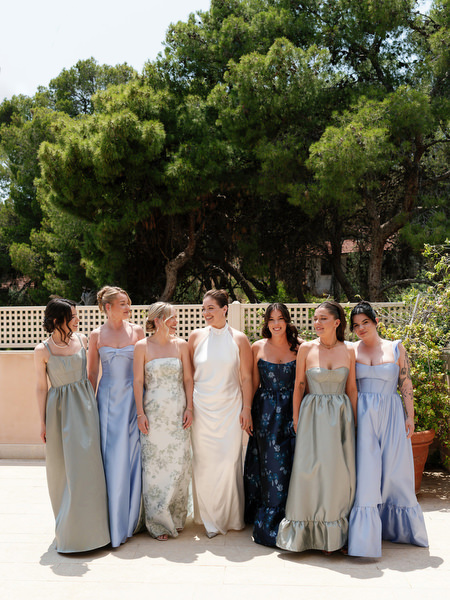 Bride surrounded by bridesmaids in soft blue and floral dresses on terrace