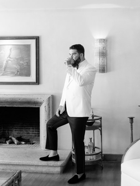 Groom sipping drink in white tuxedo jacket before ceremony at Margi luxury hotel