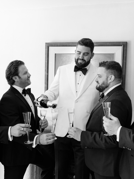 Groom pouring champagne for friends during celebration before ceremony at Margi luxury hotel
