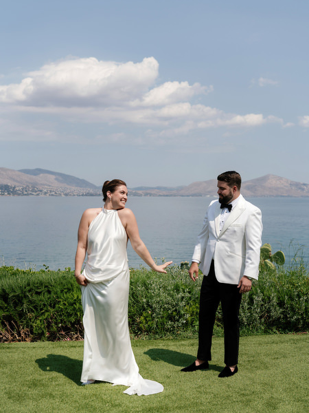 Bride and groom facing each other on cliffside lawn overlooking the Athenian Riviera