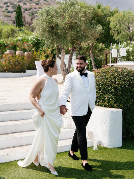 Bride and groom walking hand-in-hand across sunlit lawn before ceremony