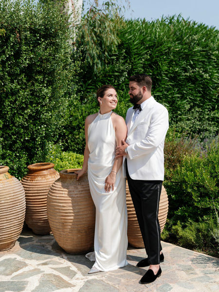 Bride and groom standing beside terracotta urns and lush greenery