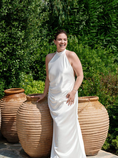 Bride smiling beside large clay urns in Mediterranean garden setting