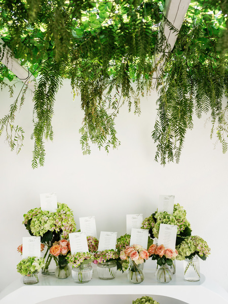 Ketubah cards displayed in glass vases beneath cascading greenery installation