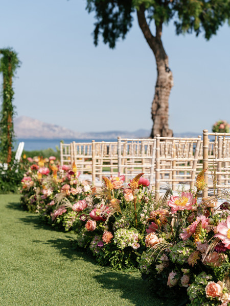 Coral and blush aisle florals lining white chairs on seaside lawn at Residence venue