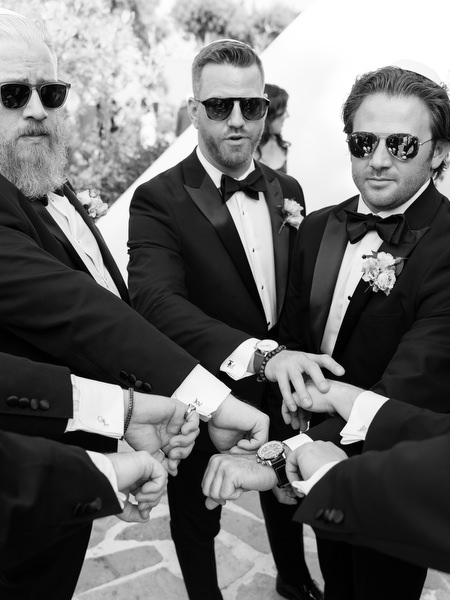 Groom and groomsmen stacking hands in black tuxedos before ceremony