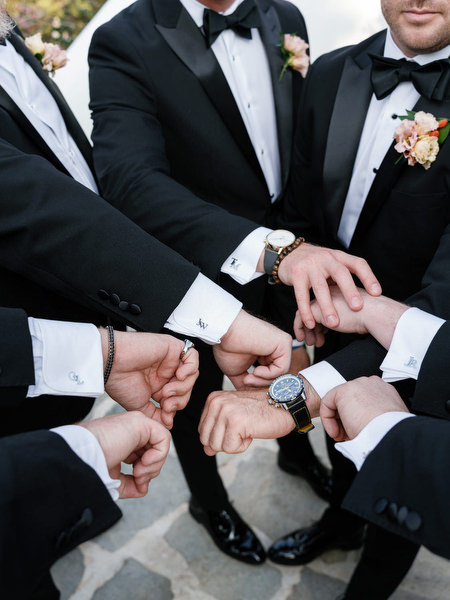 Groom and groomsmen stacking hands in black tuxedos before ceremony