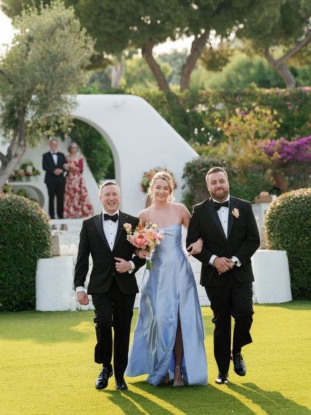 Bridesmaid walking down floral aisle surrounded by vibrant Mediterranean blooms at Island Residence
