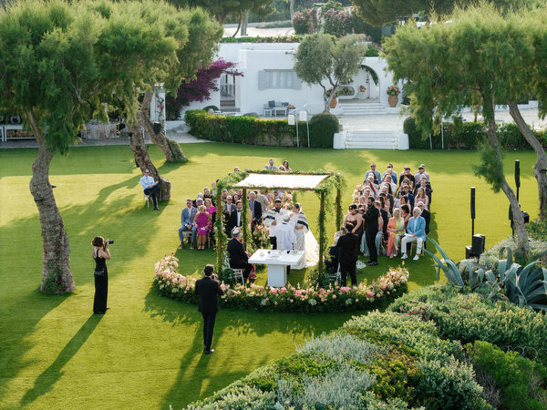 Drone perspective of guests seated on manicured lawn with chuppah centered by the coastline at Island Residence