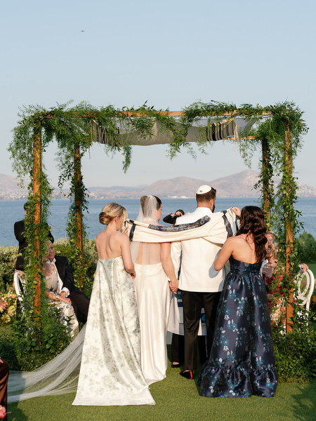 Immediate family gathered beneath greenery chuppah with sea in background