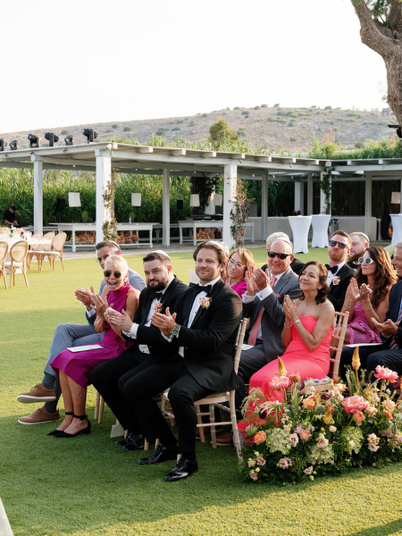 Family and friends clapping from gold chairs as the ceremony builds toward its final moment