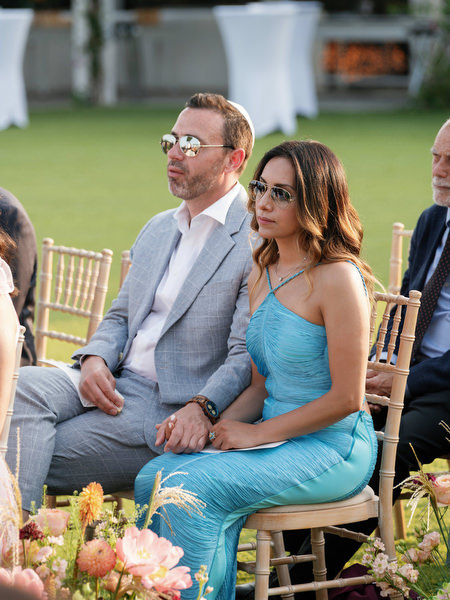 Close-up of guests seated along the floral aisle, focused on the ceremony