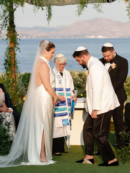 Groom stepping on the glass beneath the chuppah as family stands close