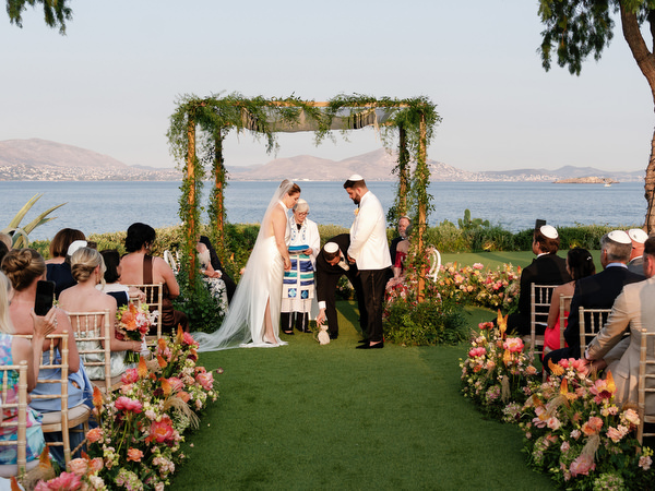 Groom stepping on the glass beneath the chuppah as family stands close
