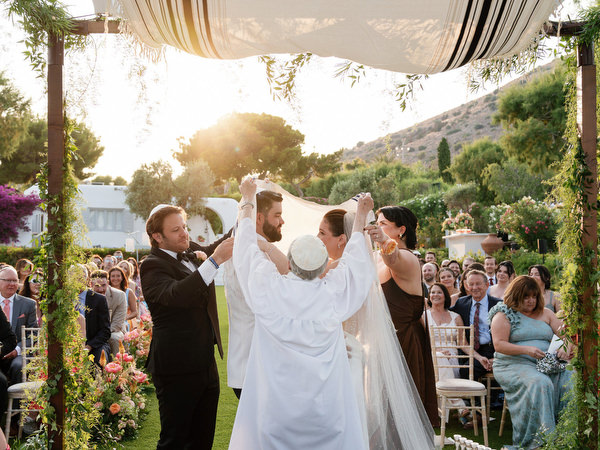 Bride and groom kissing beneath greenery-framed chuppah against the sea at Island Residence