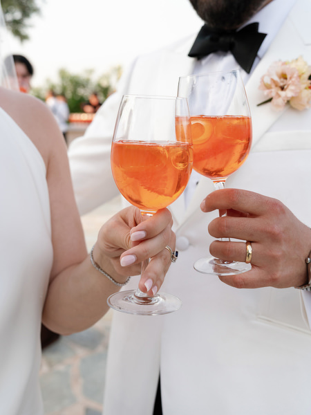 Bride and groom holding vibrant orange Aperol spritz cocktails during golden hour at Island Residence