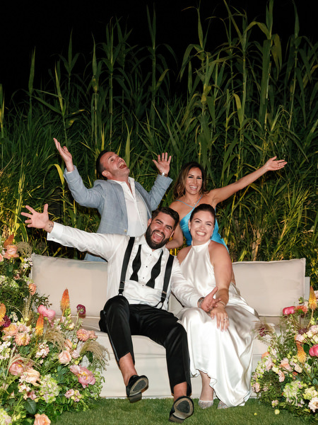 Bride and groom seated on floral-lined lounge sofa with friends celebrating at Island Residence