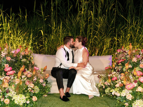 Bride and groom sharing a quiet kiss framed by florals and tall greenery