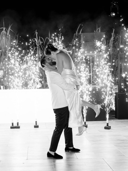 Groom lifting bride with spark fountains glowing behind them