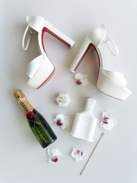 Bridal details including white heels, perfume, and champagne for a black-tie Athens wedding