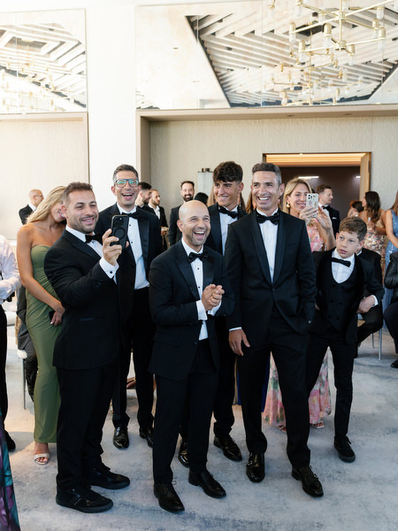 Groomsmen reacting during lively Cypriot wedding traditions at Four Seasons Astir Palace Athens