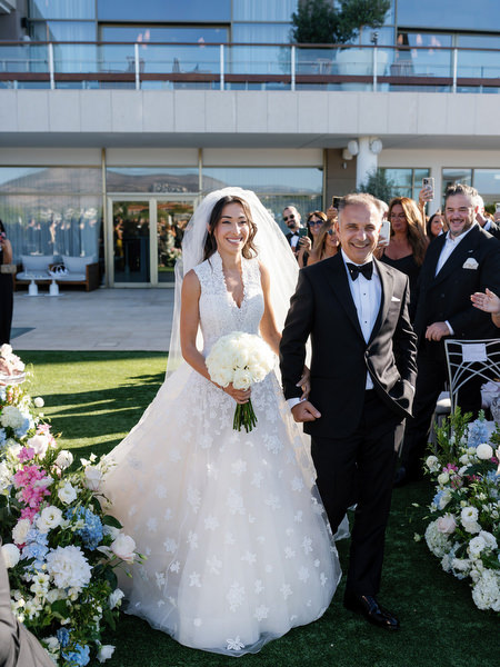 Bride walking down the aisle with her father during a seaside Athens wedding