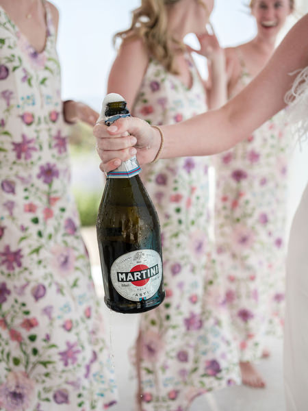 Champagne bottle popping during bridal prep at Petra Farm wedding in Paros Greece.