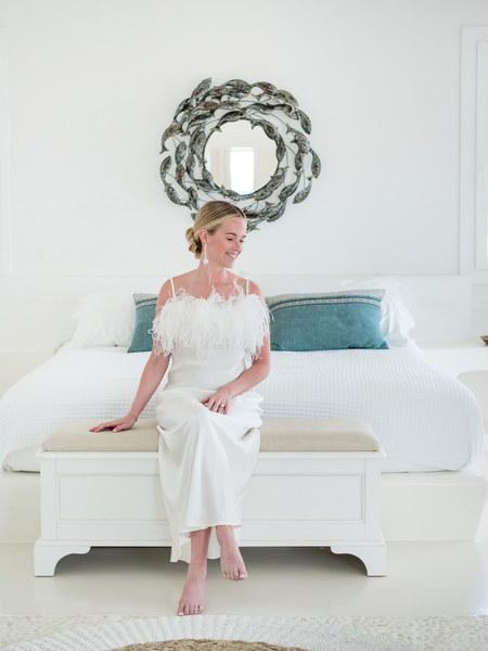 Bride sitting on white bed in modern Cycladic villa at Petra Farm Paros.