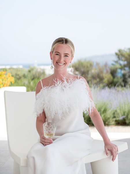 Bride in modern white gown holding champagne at Petra Farm wedding venue in Paros.