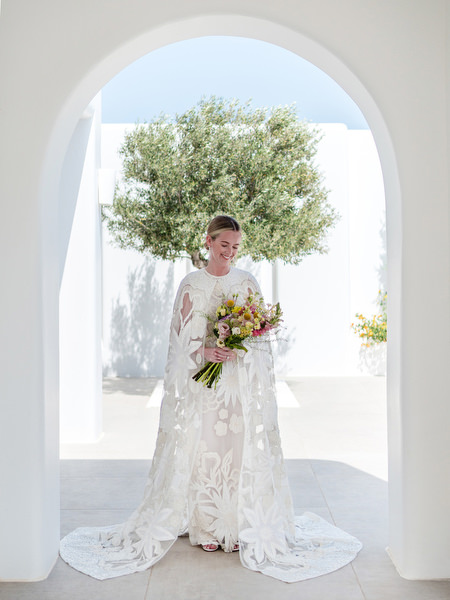 Bride holding bouquet beneath white Cycladic arch at Petra Farm Paros.