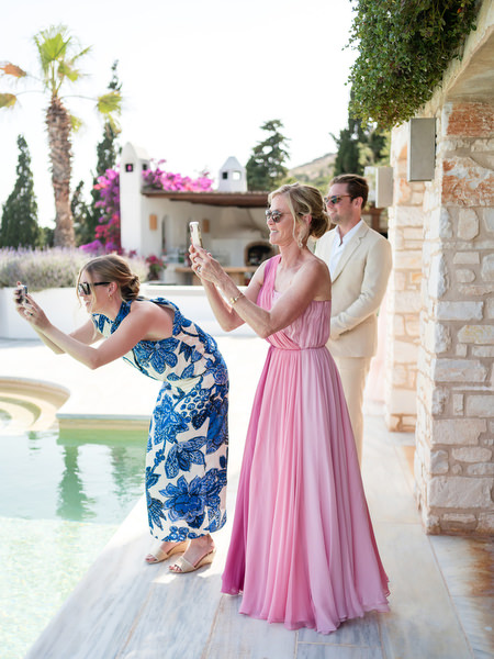 Wedding guests taking photos by pool at Petra Farm Paros overlooking the Cyclades coastline.