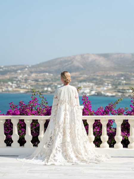 Bride in lace cape overlooking Aegean Sea at Paros Greek island wedding.