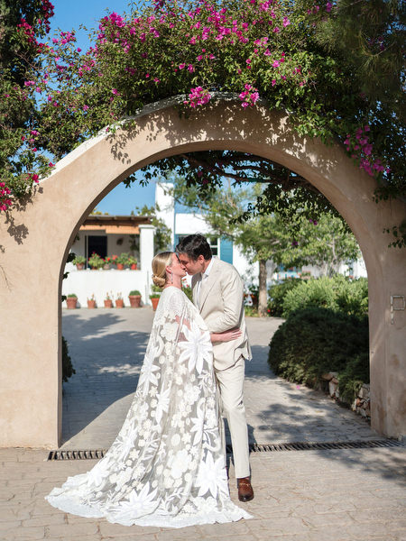 Bride and groom kissing beneath bougainvillea-covered arch at Petra Farm Paros.