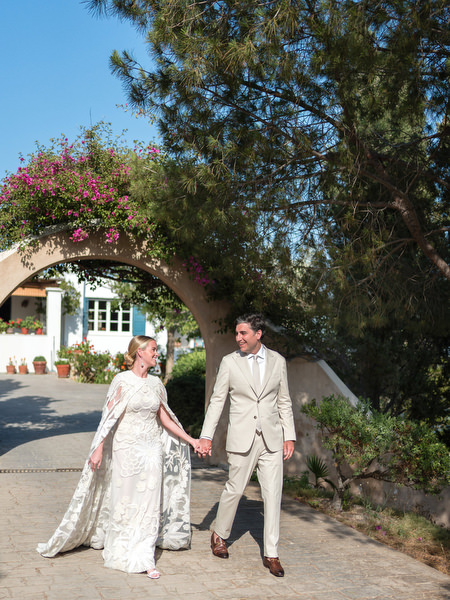 Bride and groom holding hands under trees at Paros Greek island wedding.