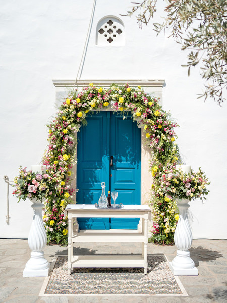 White chapel with blue door and floral arch at Petra Farm Paros wedding venue